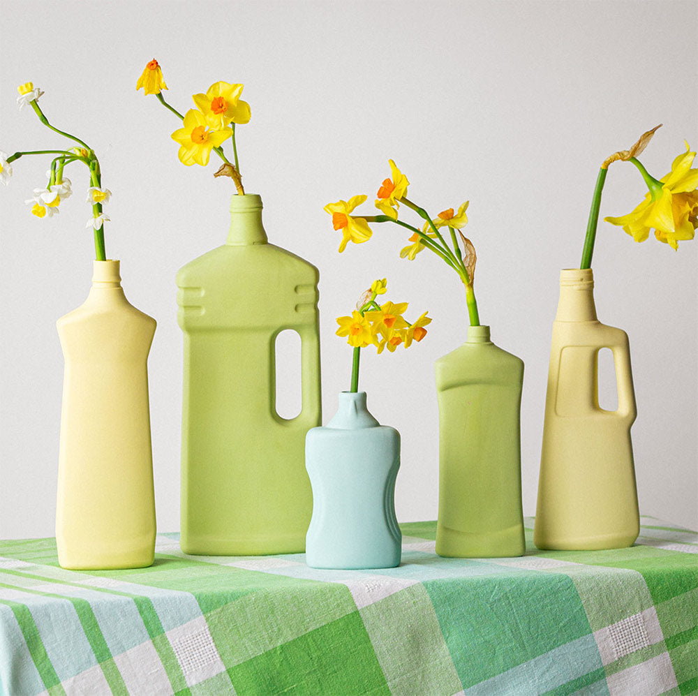 Bunte Flaschenvasen von Foekje Fleur in Gelb- und Grüntönen auf kariertem Tischtuch