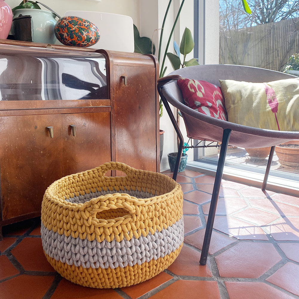 Gehäkelter Jumbokorb in den Farben mustard, light denim und honey  in Wohnzimmer vor Sideboard